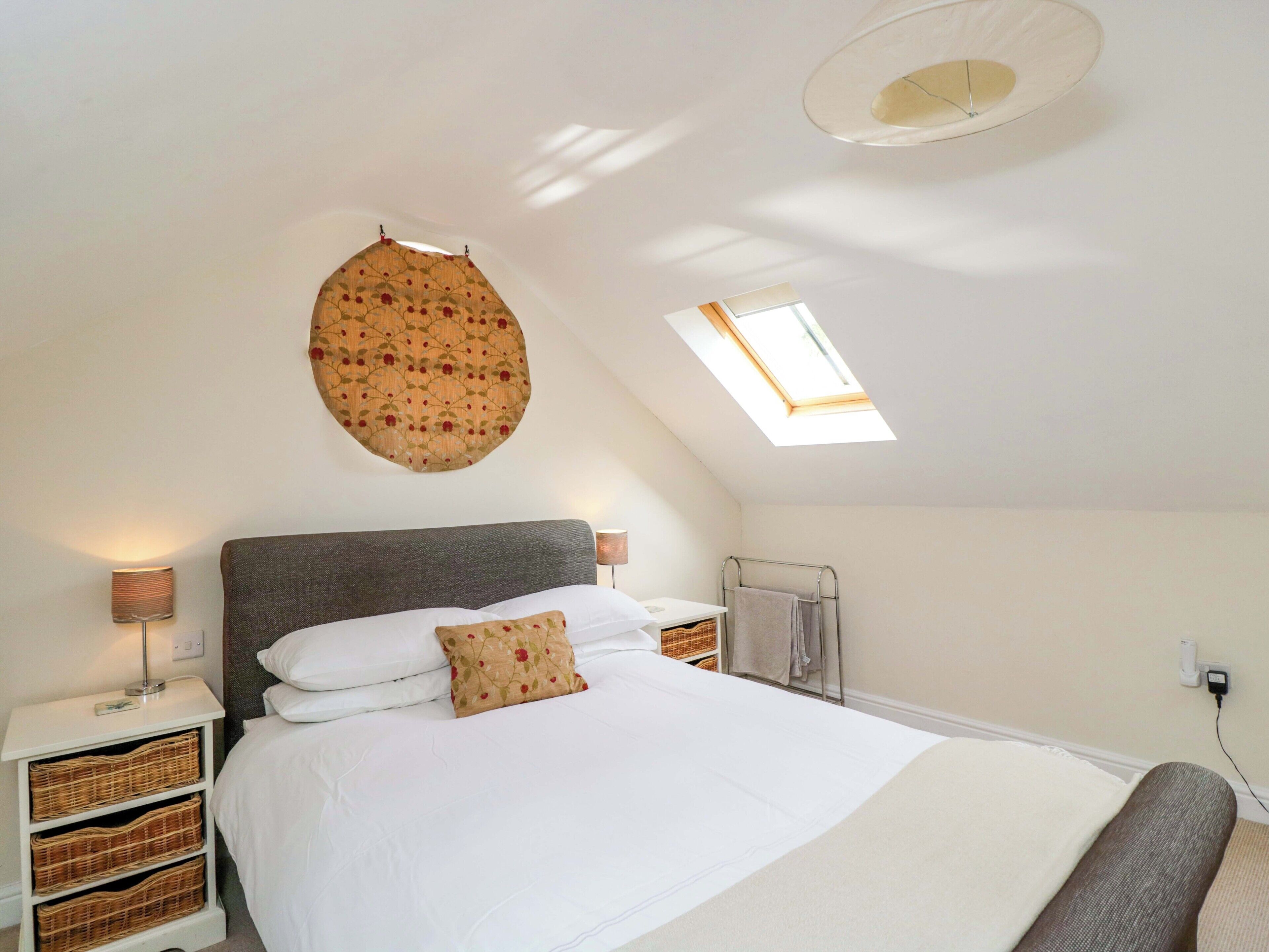A bedroom with a large bed, a skylight, a wall-mounted circular decoration, and wicker baskets under the bed.