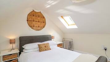 A bedroom with a large bed, a skylight, a wall-mounted circular decoration, and wicker baskets under the bed.
