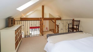 Une chambre avec un plafond en pente, un escalier en bois, un lit, une chaise et une commode blanche avec des paniers.