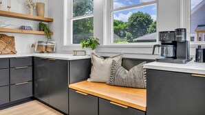 Een moderne keuken met donkere kastjes, een houten bankje en een koffiezetapparaat.