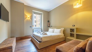 Un dormitorio con cama, sofá, televisión, ventana y estante fijado a la pared.