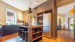 Una cocina moderna con una isla central, taburetes de bar, un refrigerador y suelo de madera.