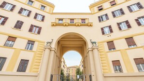 Un edificio con un arco central, varias ventanas con contraventanas y una entrada protegida por una reja.