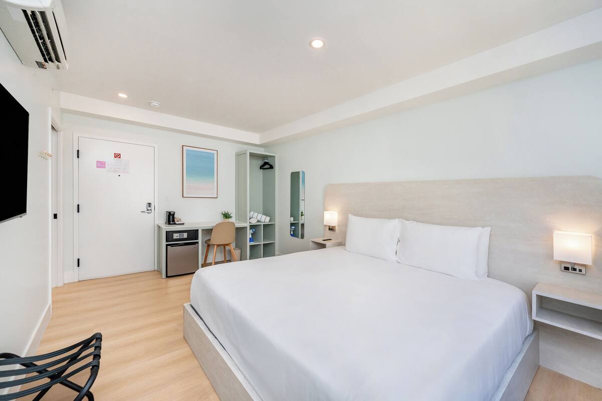 Habitación de hotel con cama, escritorio, silla, armario y televisor.