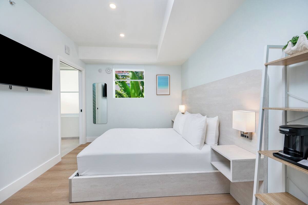 Una habitación de hotel moderna con una cama, una mesita de noche, una lámpara y una cafetera.
