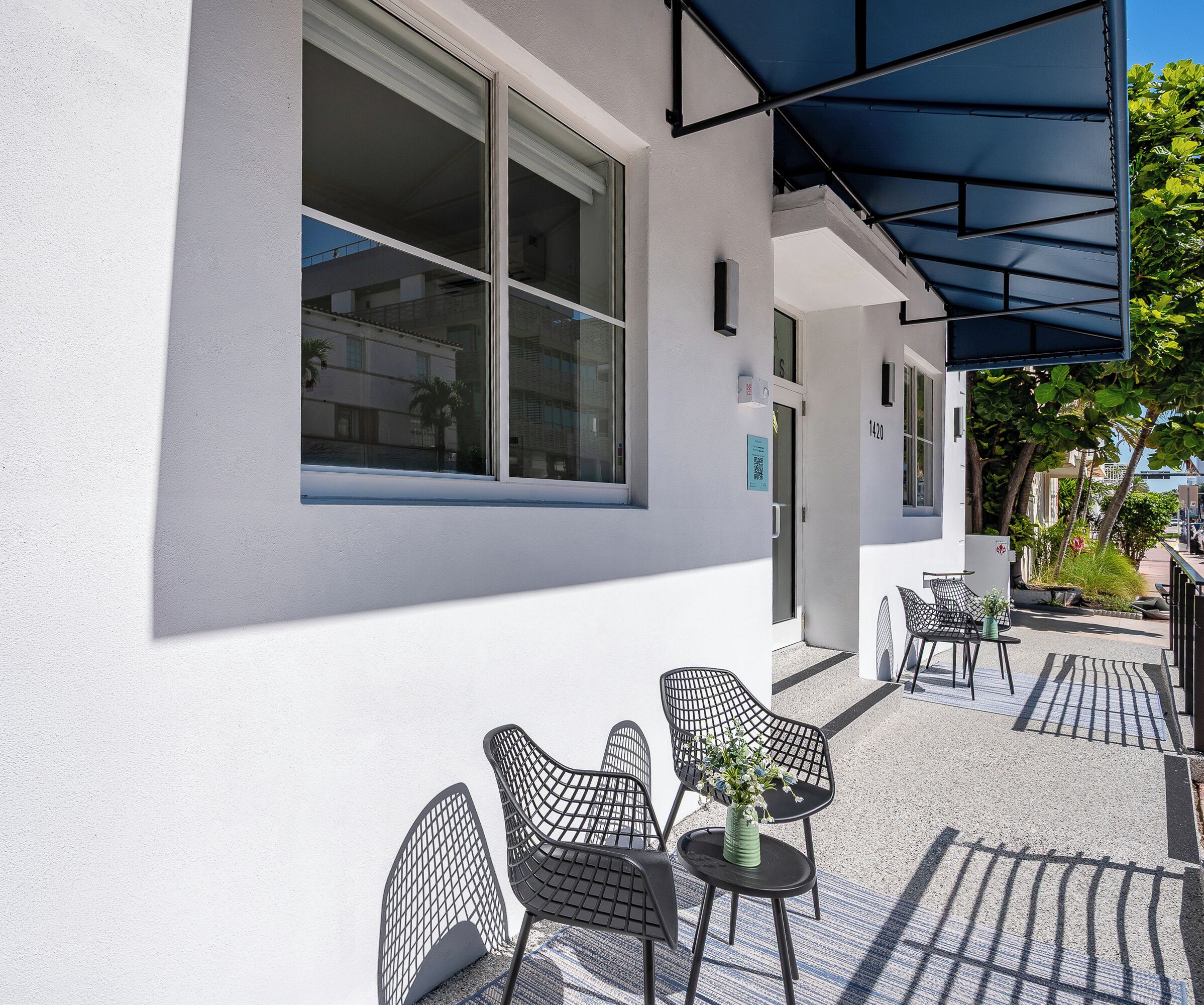 A building with large windows, outdoor seating with chairs and a table, and a covered patio area.