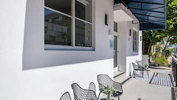 A building with large windows, outdoor seating with chairs and a table, and a covered patio area.