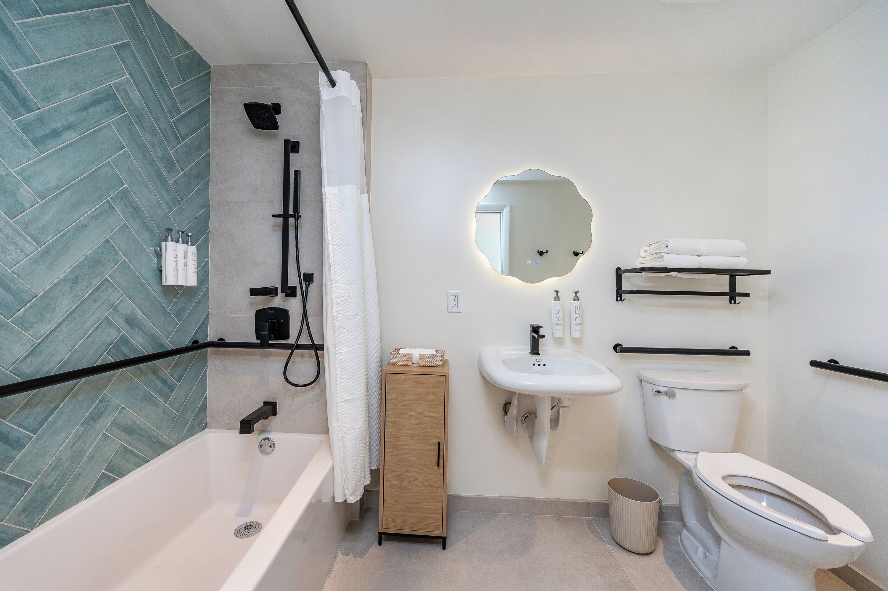 Ein modernes Badezimmer mit Badewanne, Waschbecken, Toilette und einem Spiegel mit ungewöhnlicher Form.
