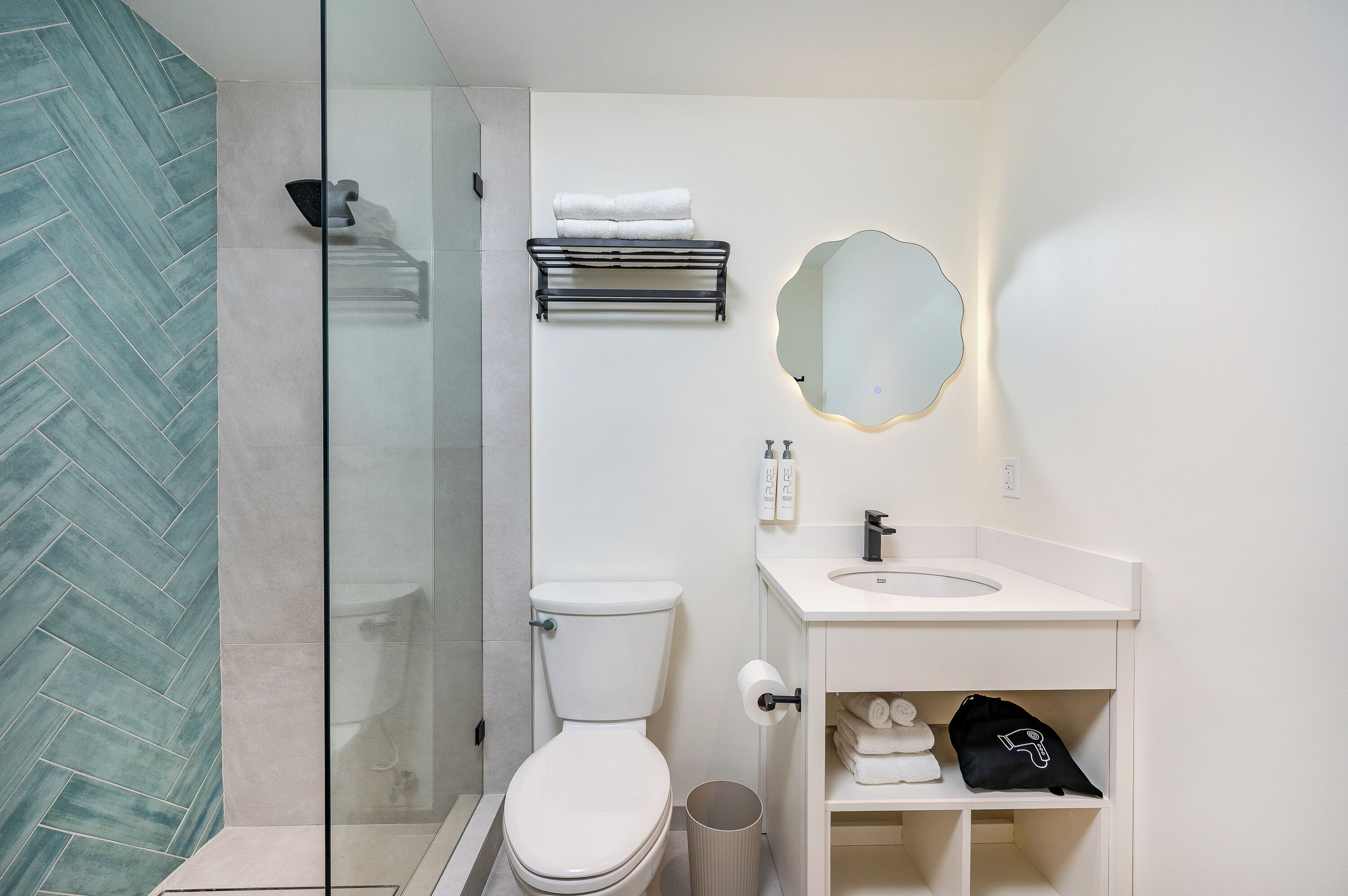 Ein modernes Badezimmer mit einer Duschkabine aus Glas, einer Toilette, einem Waschbecken mit Spiegel und einem Handtuchhalter.