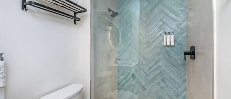 A modern bathroom with a glass shower enclosure, a toilet, and a towel rack.