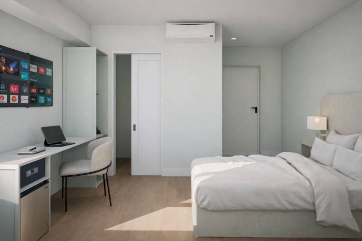 Una habitación de hotel moderna con cama, escritorio, silla y aire acondicionado de pared.