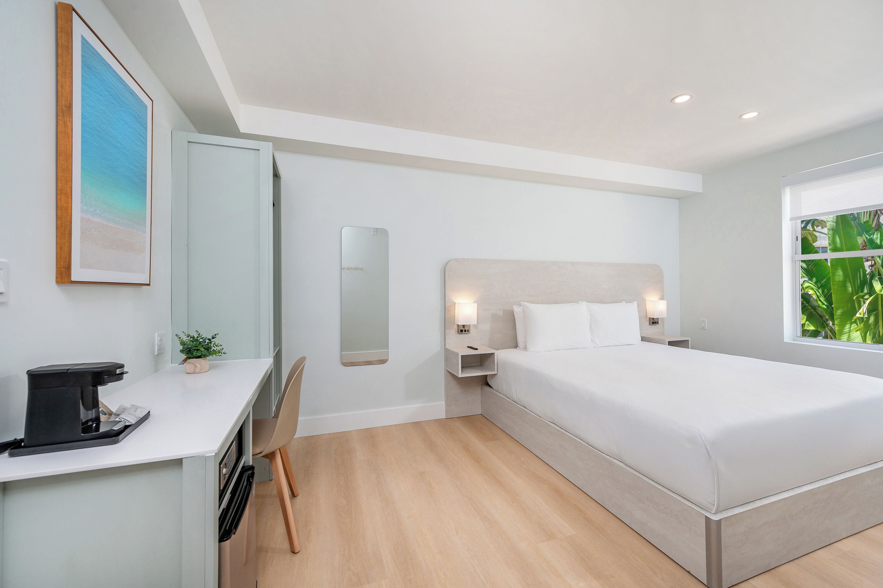 Una habitación de hotel moderna con cama, mesita de noche, escritorio, silla y ventana con vistas.
