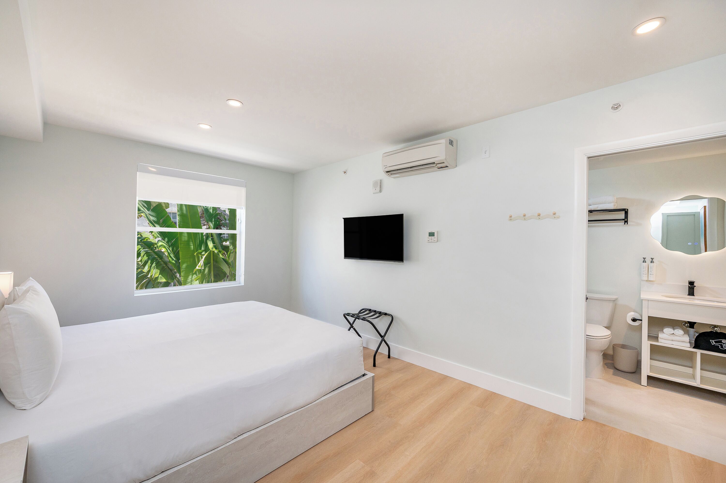 A bedroom with a bed, a window, an air conditioner, a TV, and a bathroom with a toilet and sink.