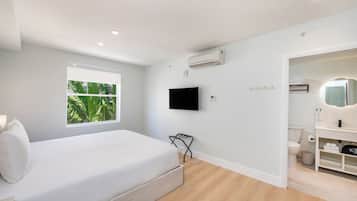 A bedroom with a bed, a window, an air conditioner, a TV, and a bathroom with a toilet and sink.