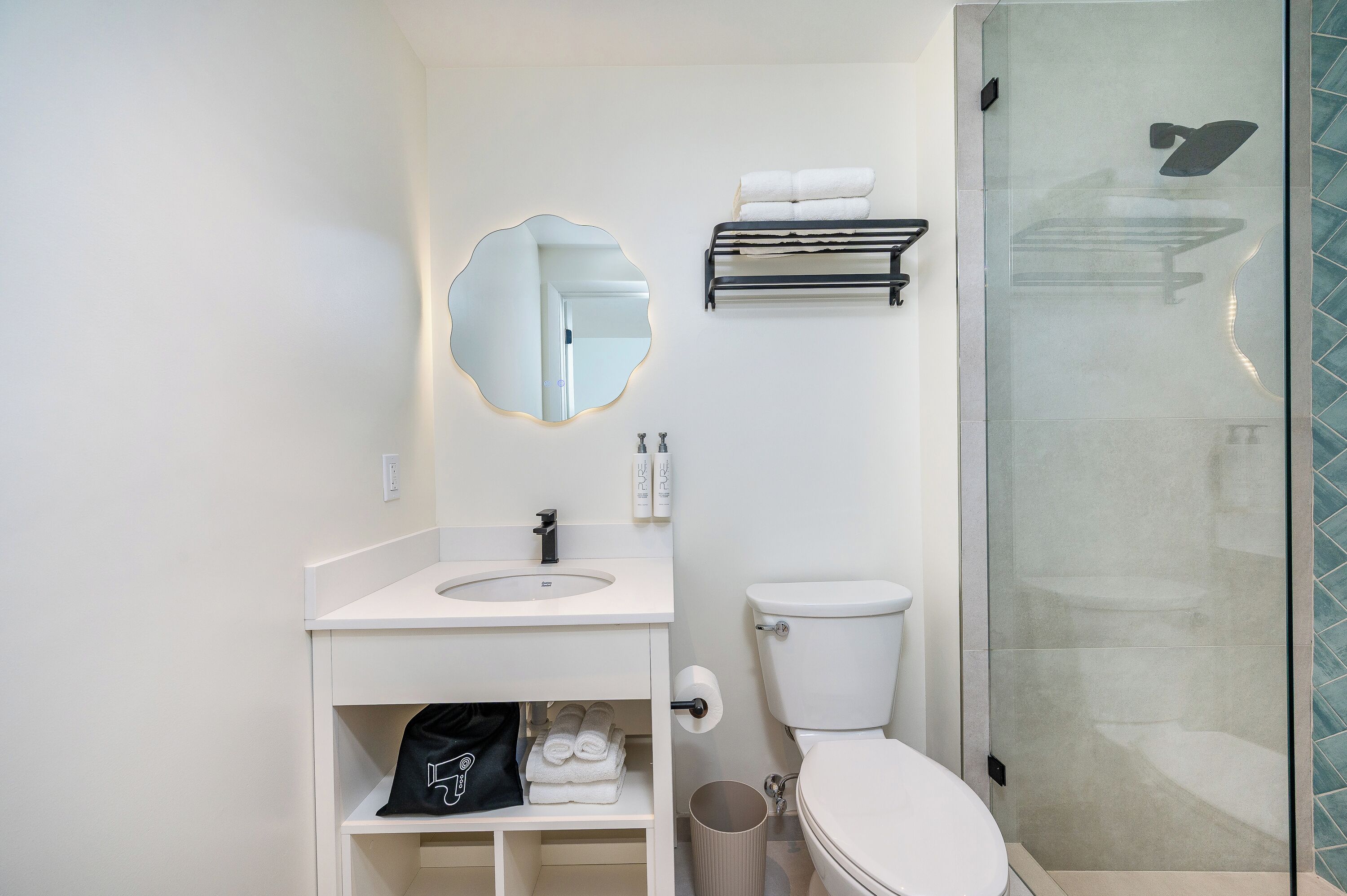 Une salle de bain avec un lavabo blanc, un miroir, un porte-serviettes, des toilettes et une cabine de douche en verre.