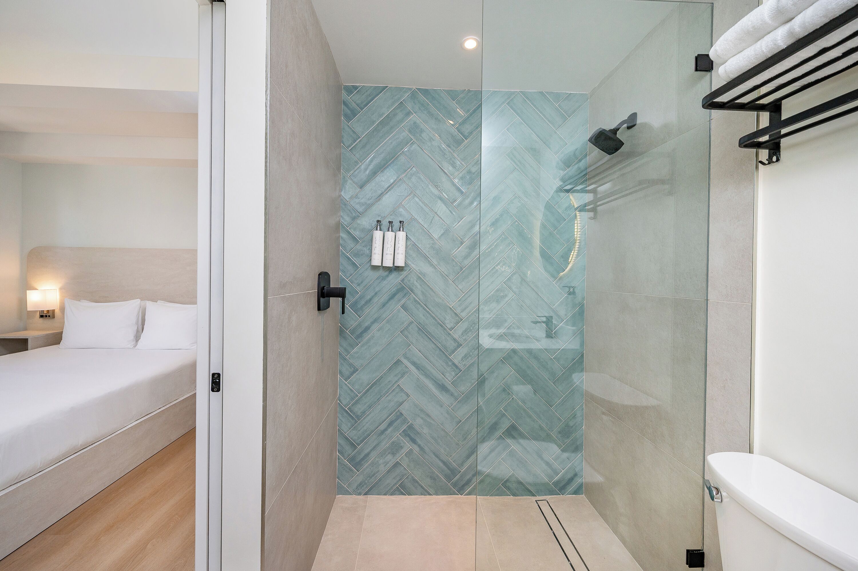Une salle de bain moderne avec une douche à parois de verre, des toilettes et un lit recouvert de linge de maison blanc.