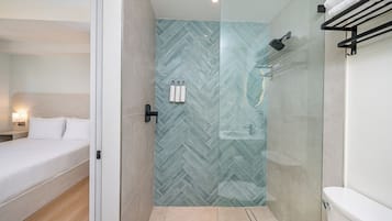 Une salle de bain moderne avec une douche à parois de verre, des toilettes et un lit recouvert de linge de maison blanc.
