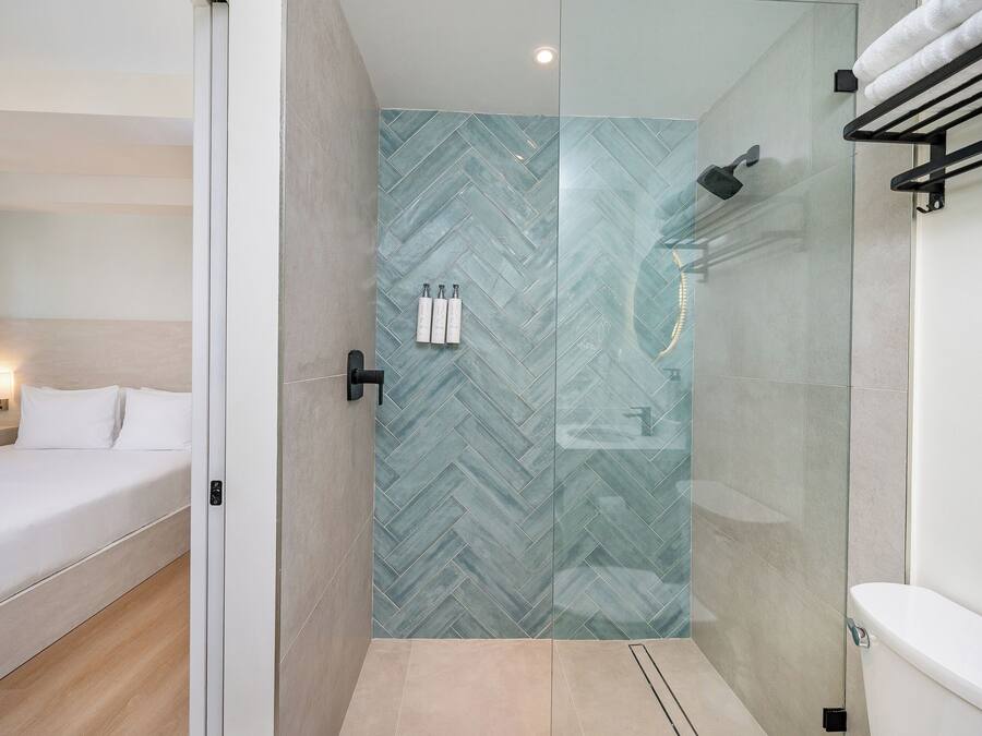 Une salle de bain moderne avec une douche à parois de verre, des toilettes et un lit recouvert de linge de maison blanc.