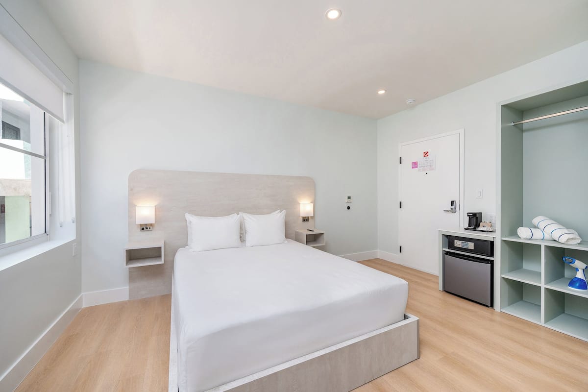 Una habitación de hotel moderna con una cama grande, mesitas de noche, un armario y una pequeña kitchenette.