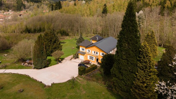 Une maison avec une allée, entourée d’arbres et de collines.