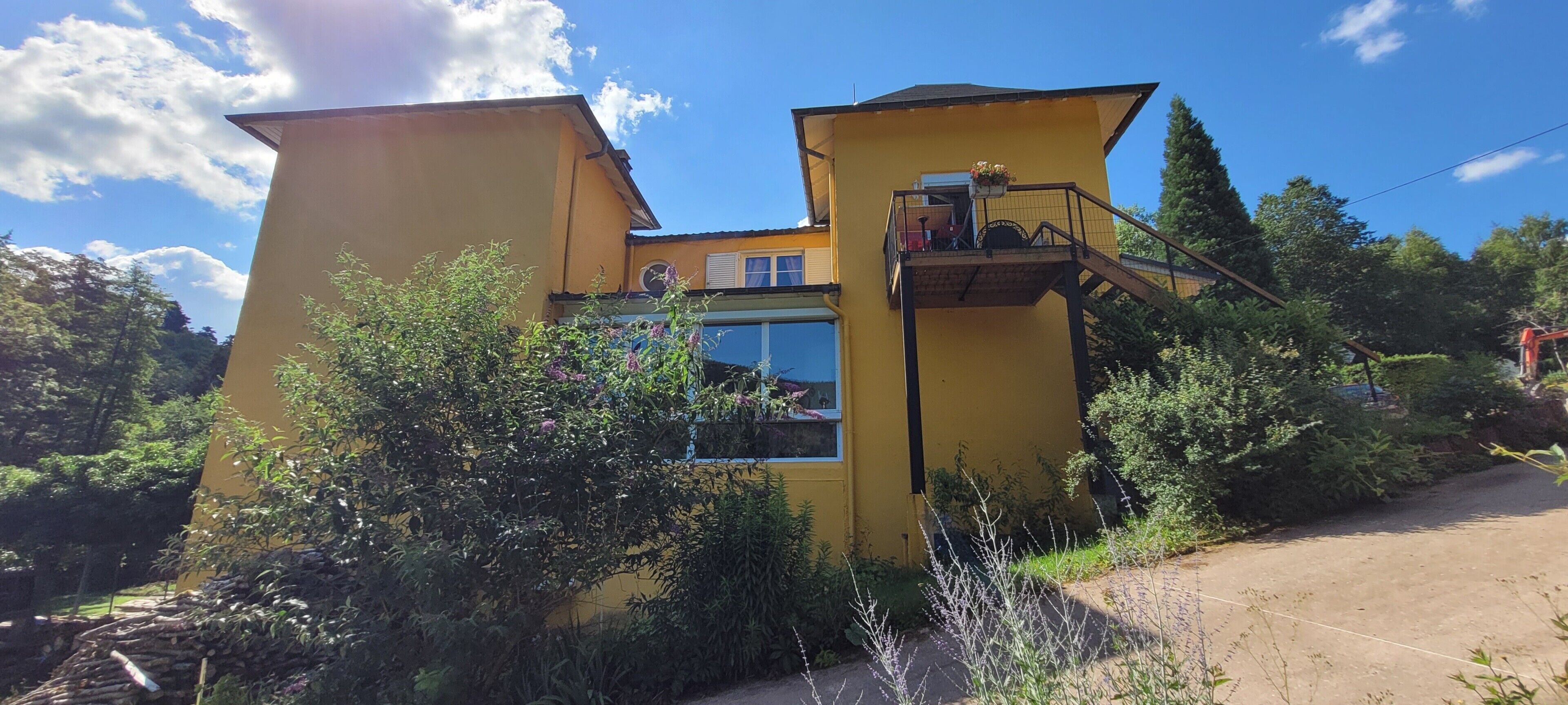 A yellow building with a balcony, surrounded by greenery.