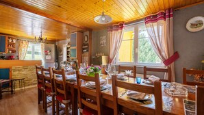 Un espace repas avec des tables et des chaises en bois, un lustre et une fenêtre avec des rideaux.