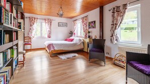 Une pièce chaleureuse avec un plafond en bois, un lit, une bibliothèque, une chaise et une fenêtre.