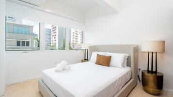 Habitación de hotel moderna con una cama grande, dos lámparas de noche, vistas de edificios por la ventana y una pared blanca.