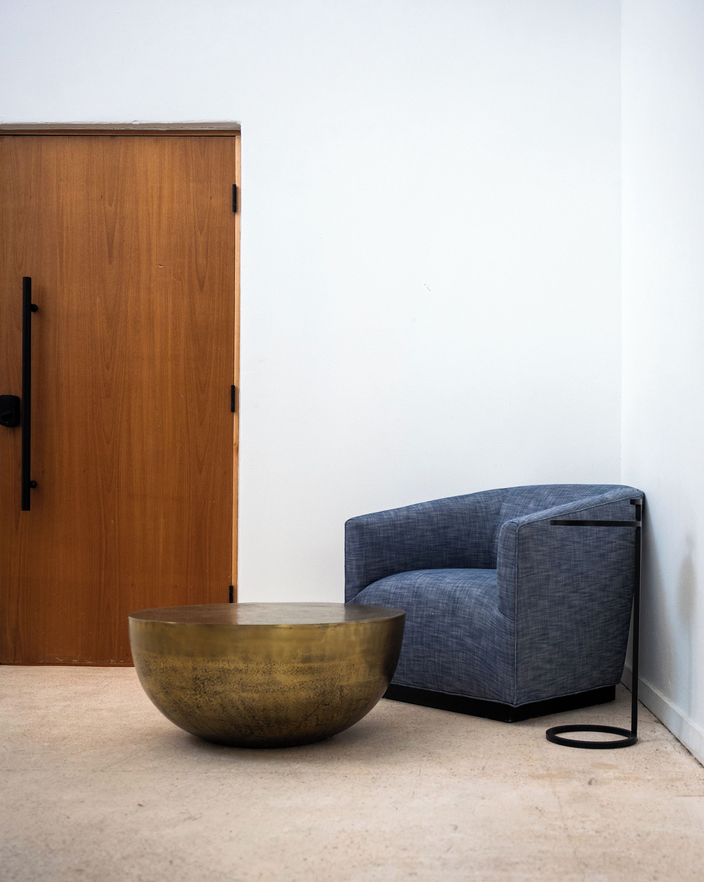 A room with a wooden door, a blue chair, and a large brass bowl on the floor.