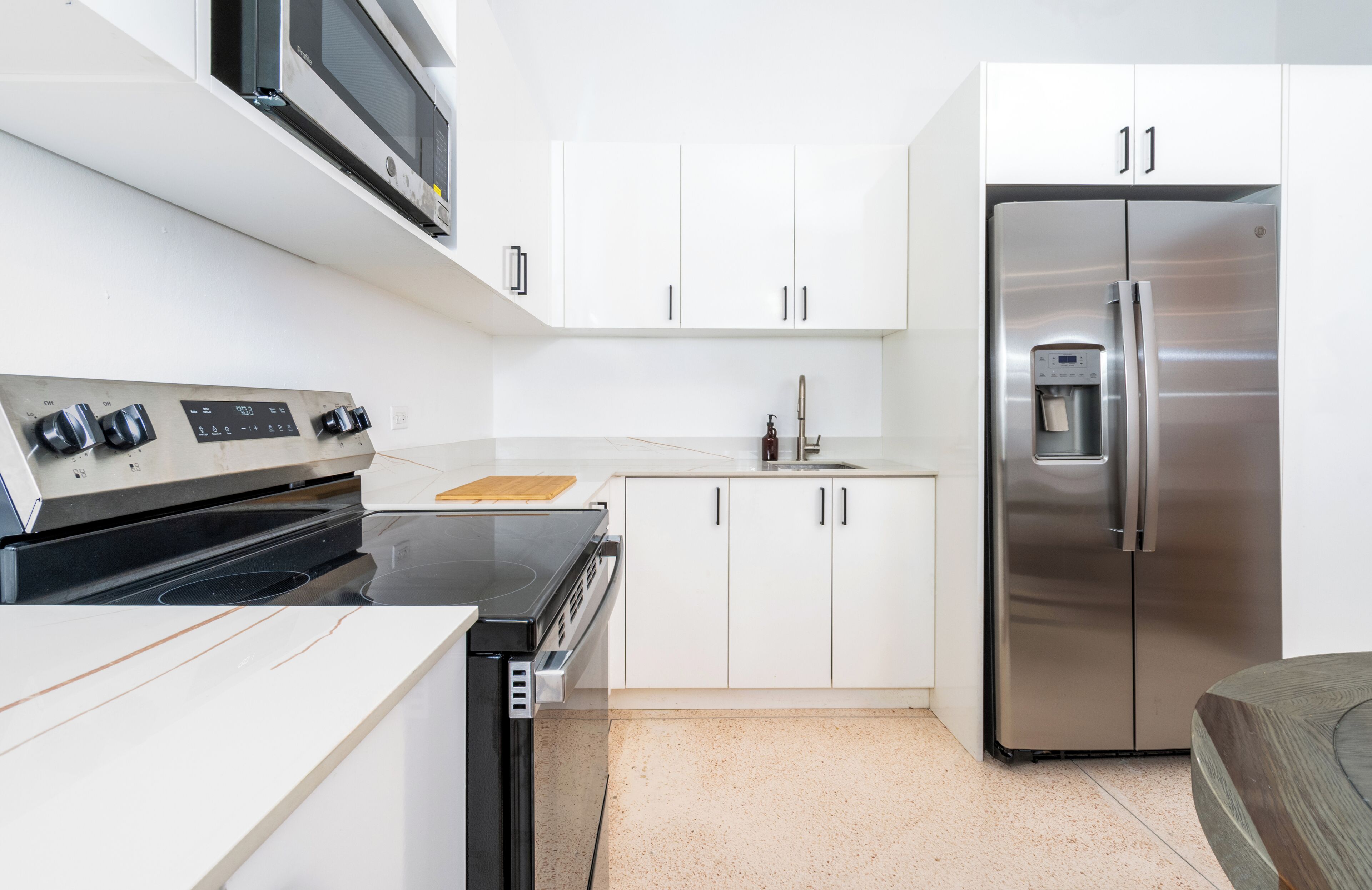 A compact kitchen with a stove, microwave, refrigerator, and white cabinets.