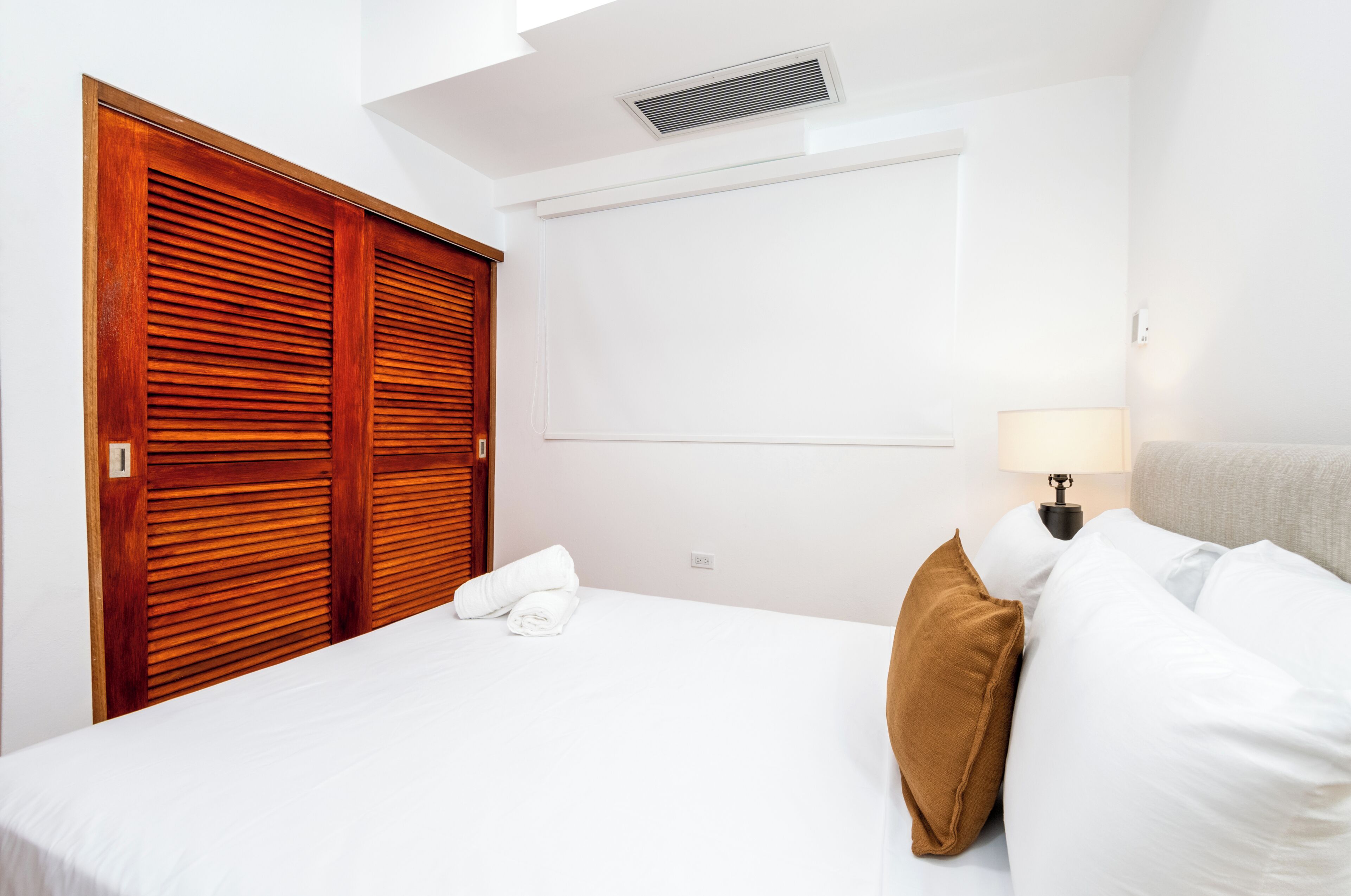 A hotel room with a bed, a wooden wardrobe, a bedside lamp, and a window.