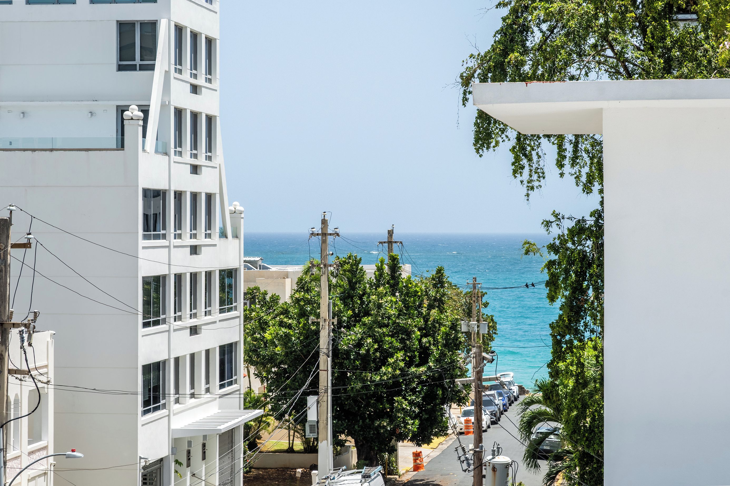 Un paisaje urbano costero con edificios modernos, una vista despejada del mar y una calle con coches aparcados.