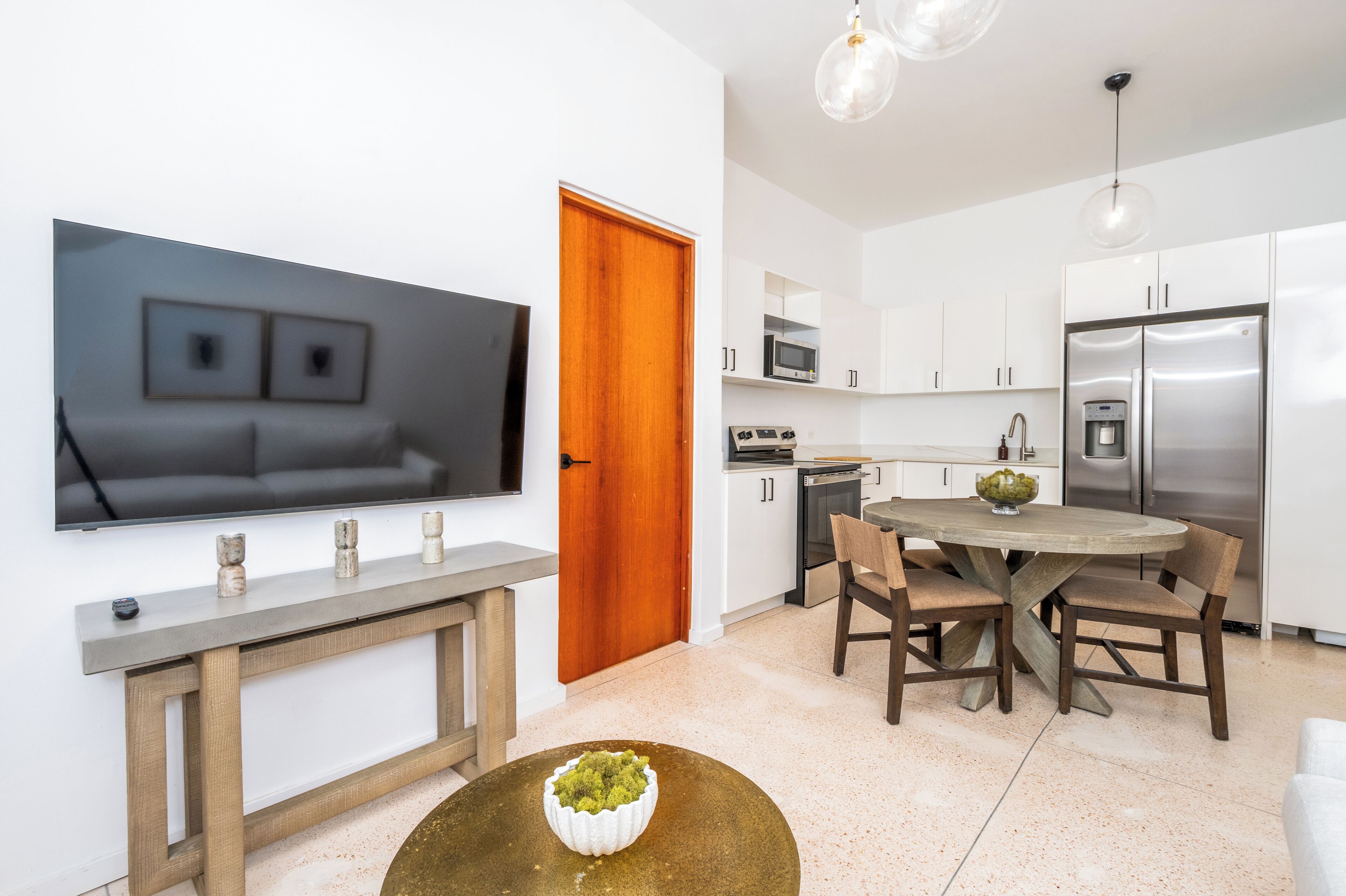A modern kitchen with white cabinets, stainless steel appliances, and a dining area with a round wooden table and chairs.