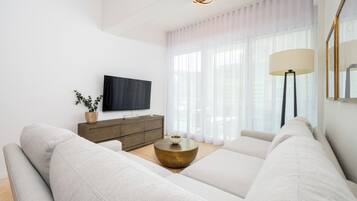 A modern living room with a large sofa, a coffee table, a TV, and a lamp.