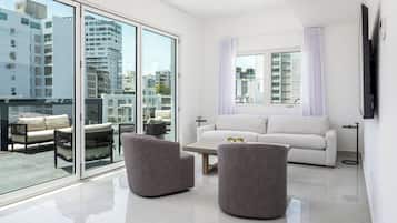 A modern living room with a white sofa, two grey armchairs, a coffee table, and a large window with a view of city buildings.
