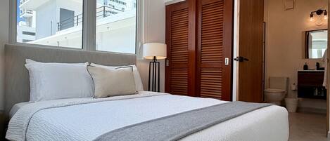 Une chambre d’hôtel avec un grand lit, une lampe de chevet, une armoire en bois et une vue sur le paysage urbain par la fenêtre.