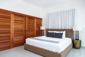 A bedroom with a large bed, two bedside lamps, a wooden wardrobe, and a window with curtains. - Ashford Apartments (San Juan)