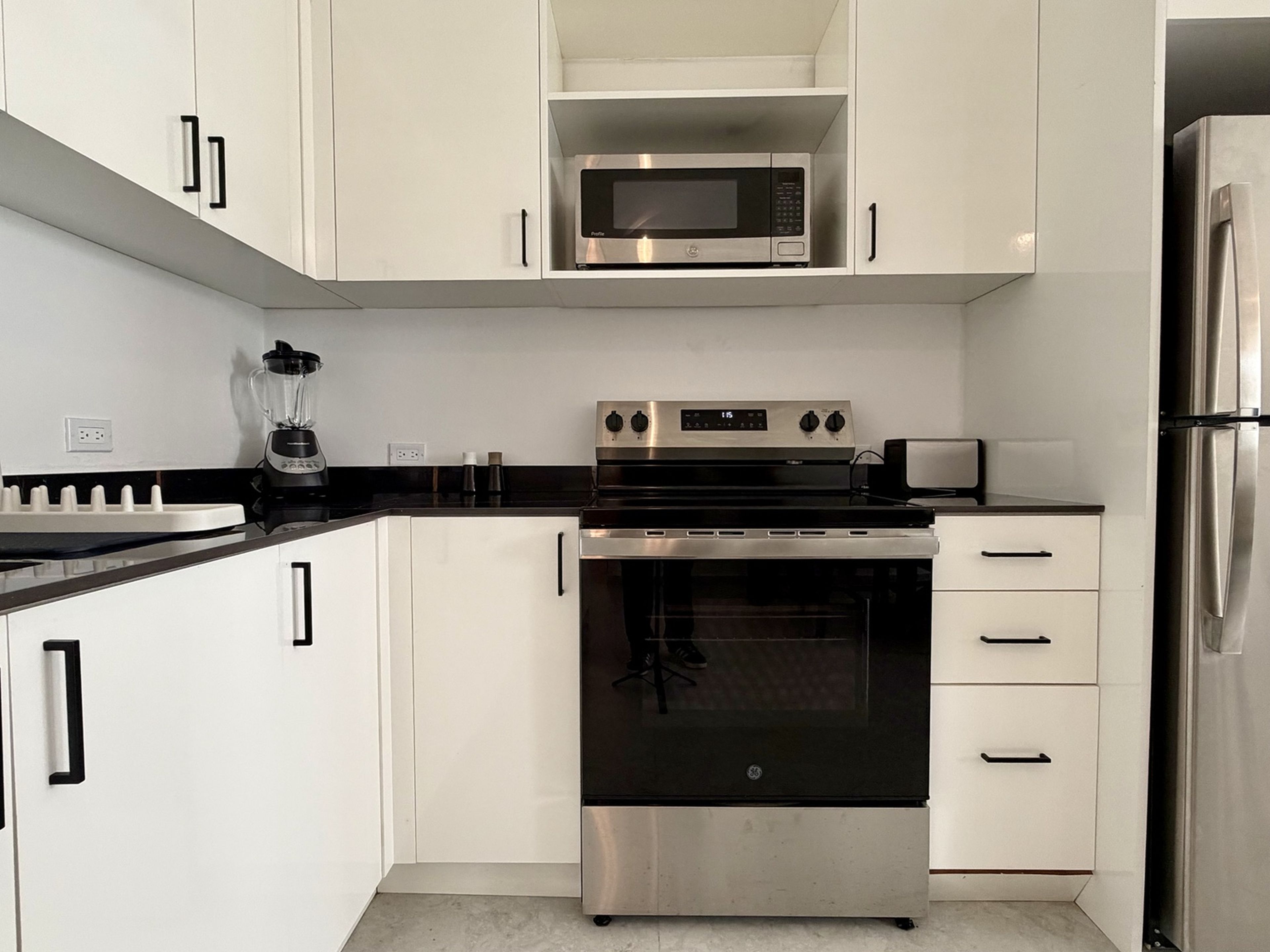 Een moderne keuken met witte kasten, een stalen magnetron, een inbouwoven en een koelkast.