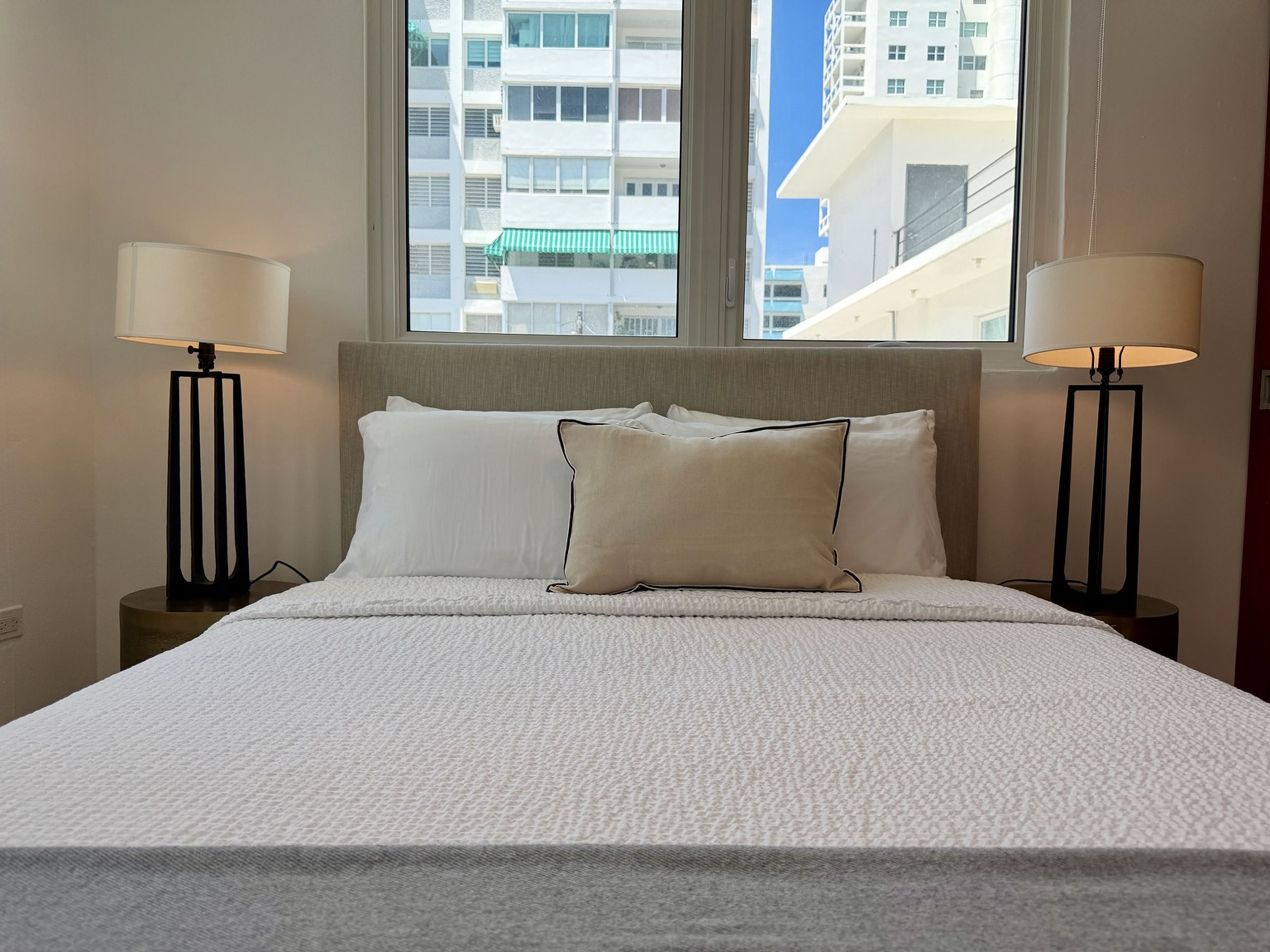Een hotelkamer met een groot bed, twee bedlampen, een raam met uitzicht op gebouwen, en een hoofdbord.