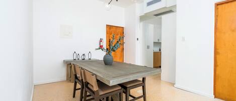 A dining area with a wooden table, chairs, a vase with flowers, and a modern chandelier.
