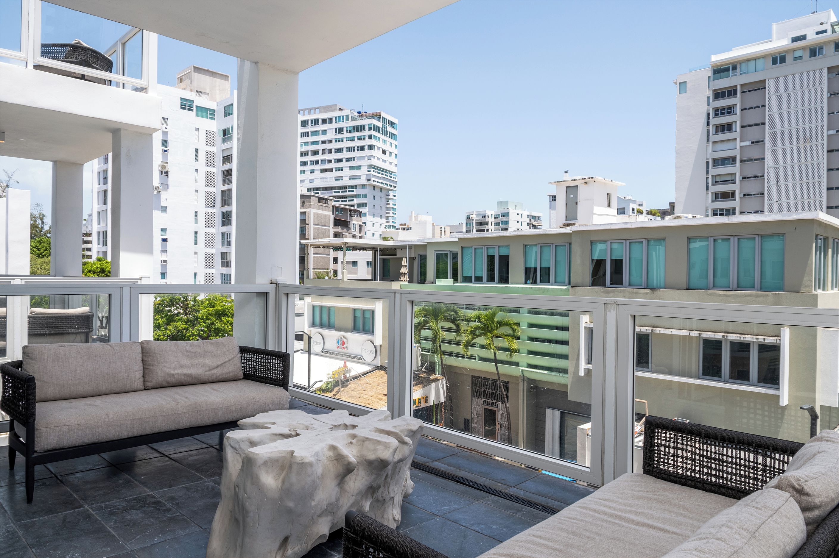 Un balcone con mobili da esterno, vista sulla città e un edificio con un cartello che recita 'PERONI'.