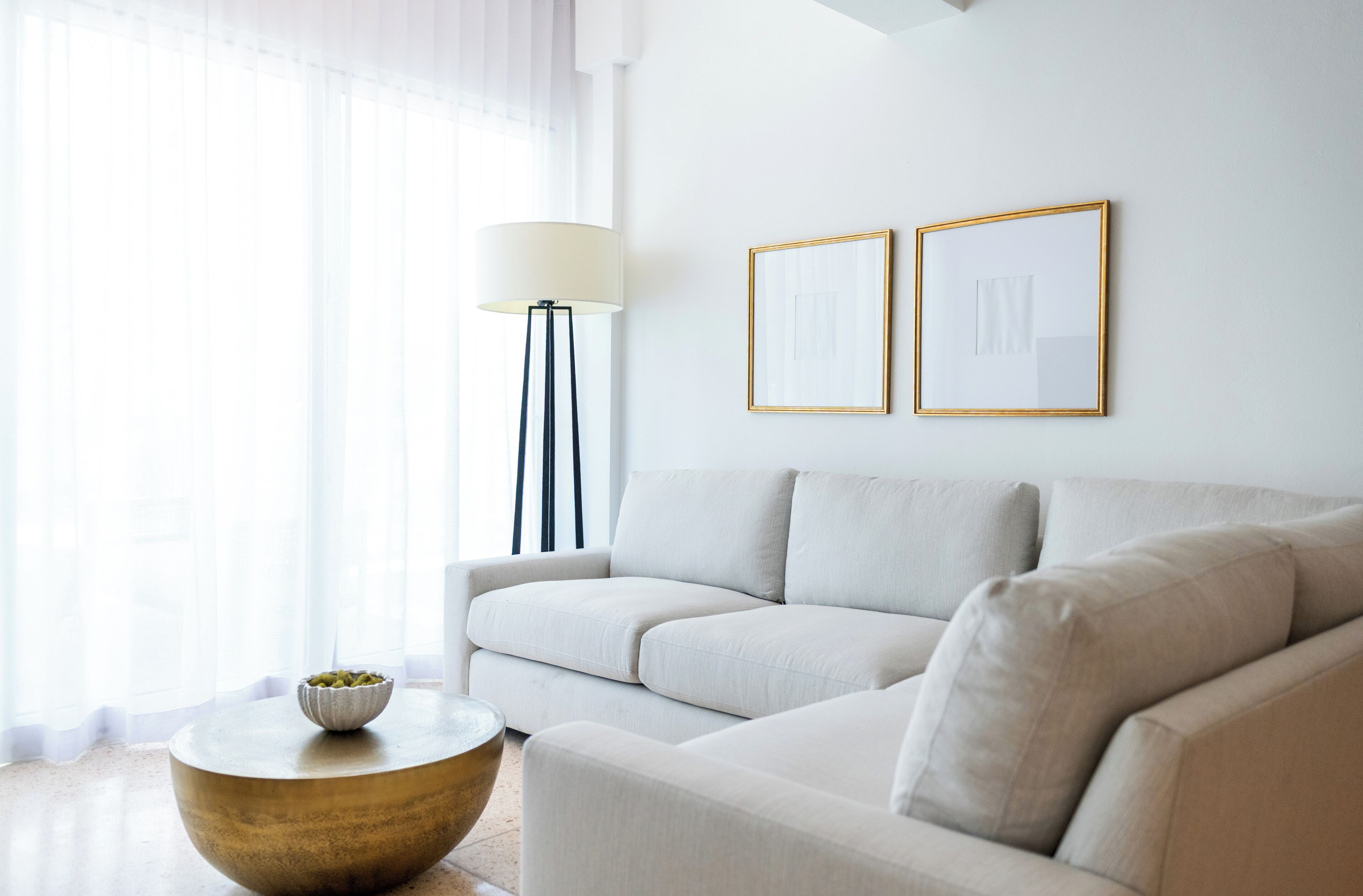 Een moderne woonkamer met een bank, een ronde salontafel en een vloerlamp. Twee ingekaderde foto's hangen aan de muur.