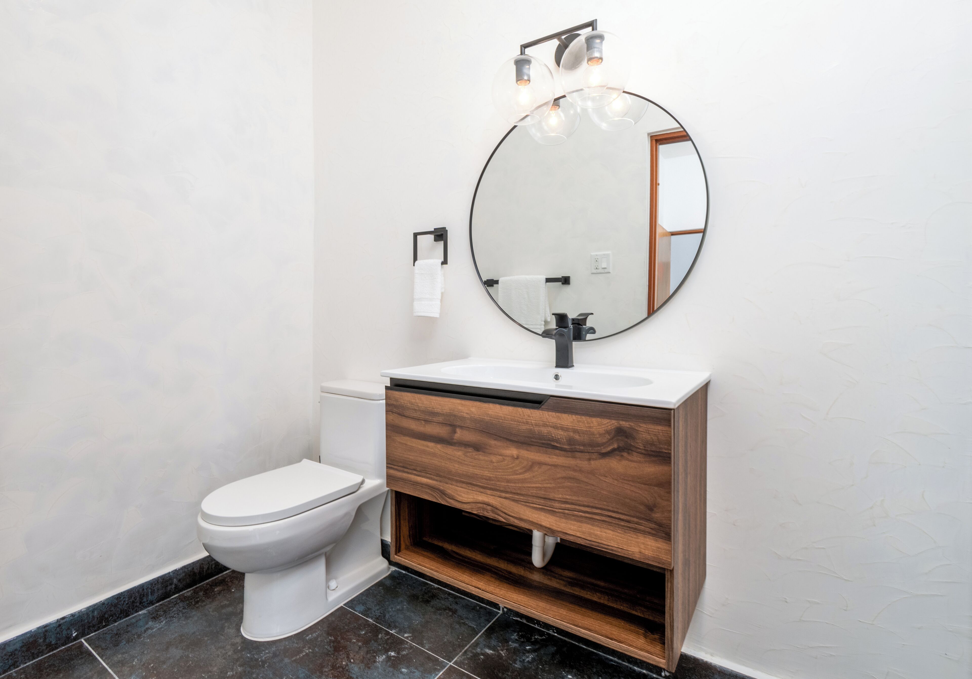 Une salle de bain avec des toilettes blanches, un meuble-lavabo en bois avec un miroir et un lavabo blanc.