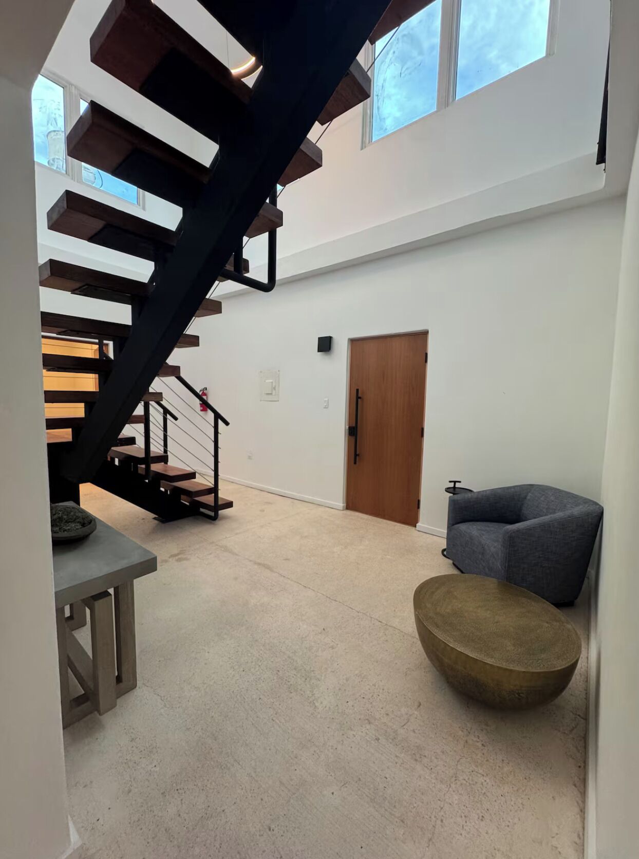 A spacious living area with a modern staircase, a wooden door, and a grey armchair.
