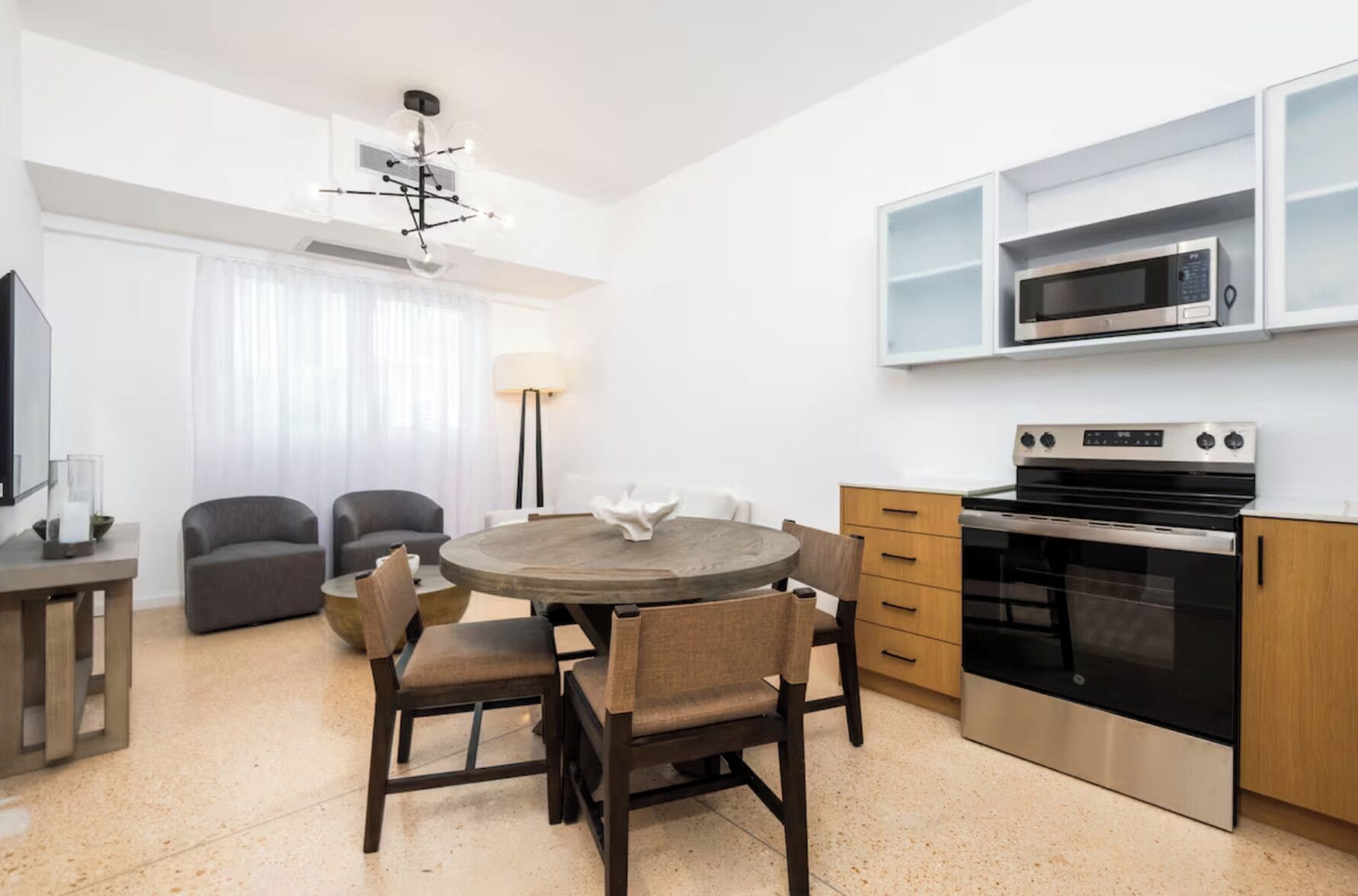 Cocina moderna con microondas integrado, horno y armarios de madera. Cuenta con una zona de comedor con una mesa redonda y sillas.