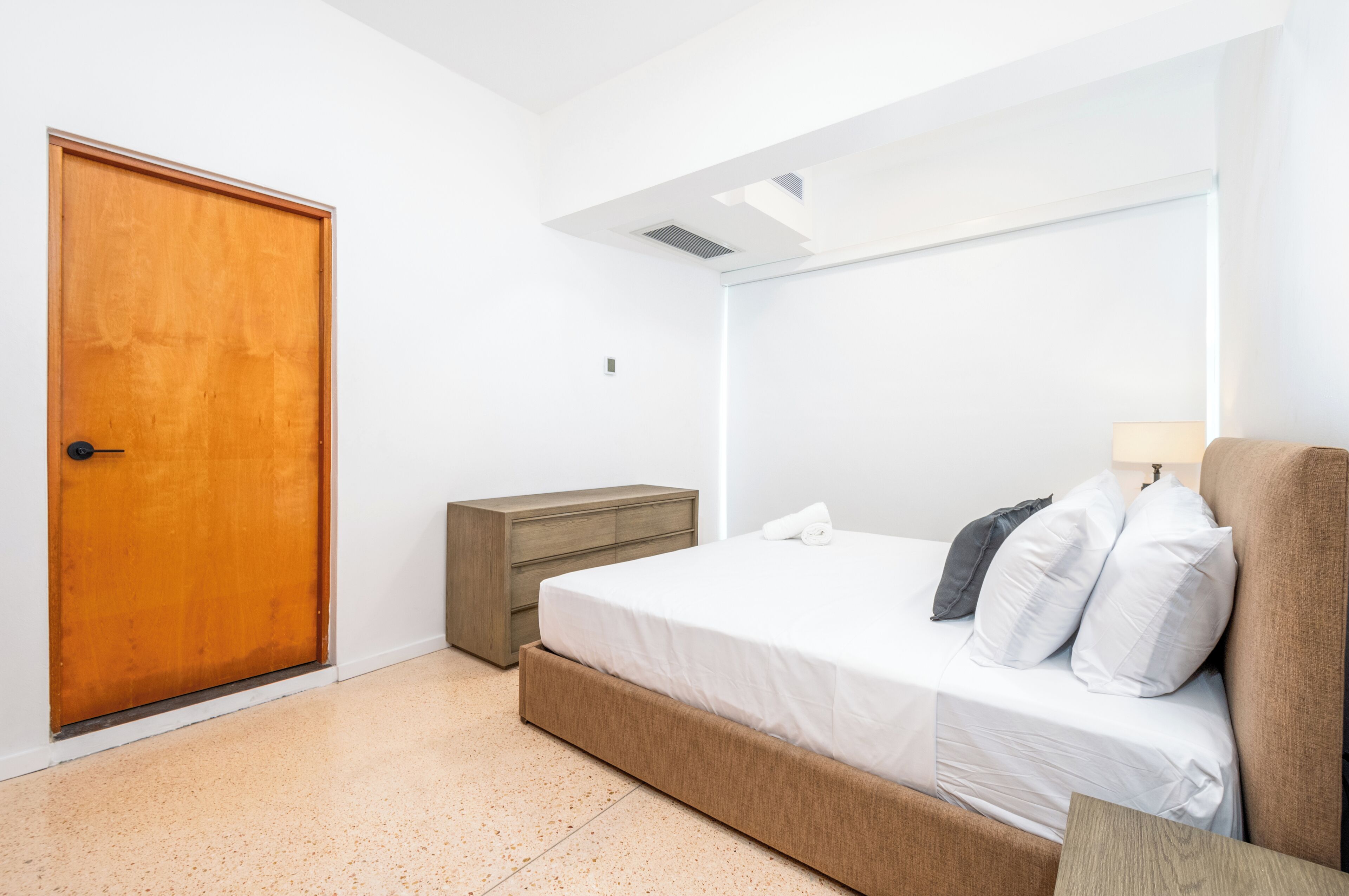 A bedroom with a wooden door, a bedside table, a bed with pillows, and a nightstand.