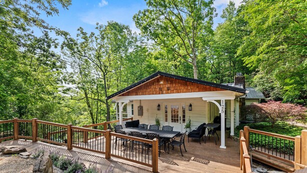 A wooden deck with outdoor furniture, surrounded by lush greenery and trees. - 7 BDR Retreat w Guest Houses Waterfall Trail (Hendersonville)