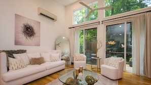 A modern living room with a glass coffee table, white sofas, a large mirror, and a painting on the wall. - 7 BDR Retreat w Guest Houses Waterfall Trail (Hendersonville)