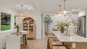 A modern kitchen with a central island, stainless steel appliances, and a dining area with a wooden table and chairs. - 7 BDR Retreat w Guest Houses Waterfall Trail (Hendersonville)