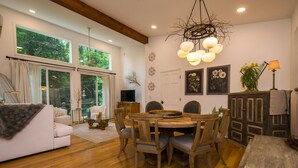 Un salon spacieux avec une grande fenêtre, un coin repas doté de meubles en bois et un lustre.
